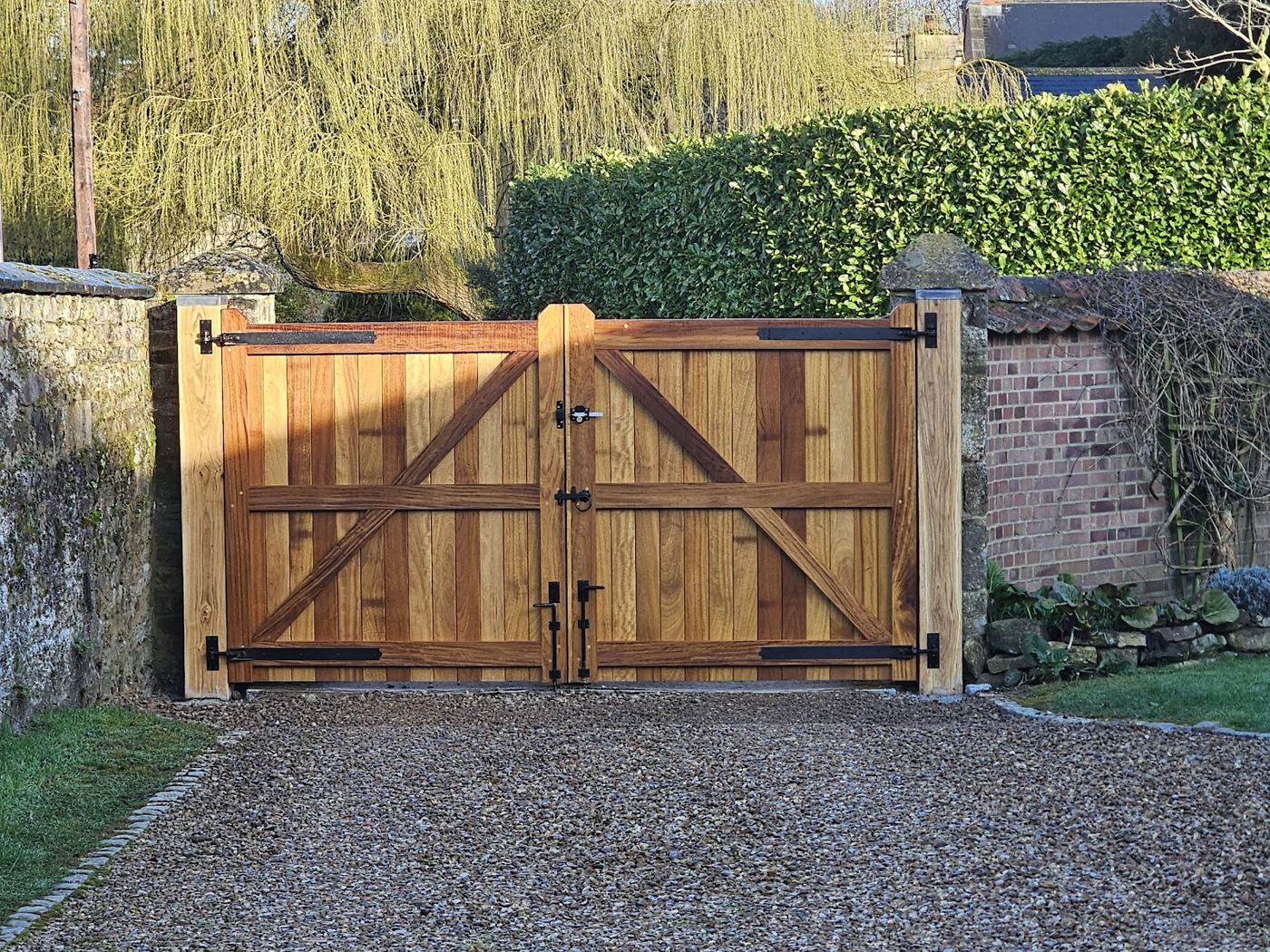 Double timber driveway gates with black strap hinges, between a hedge and a brick wall